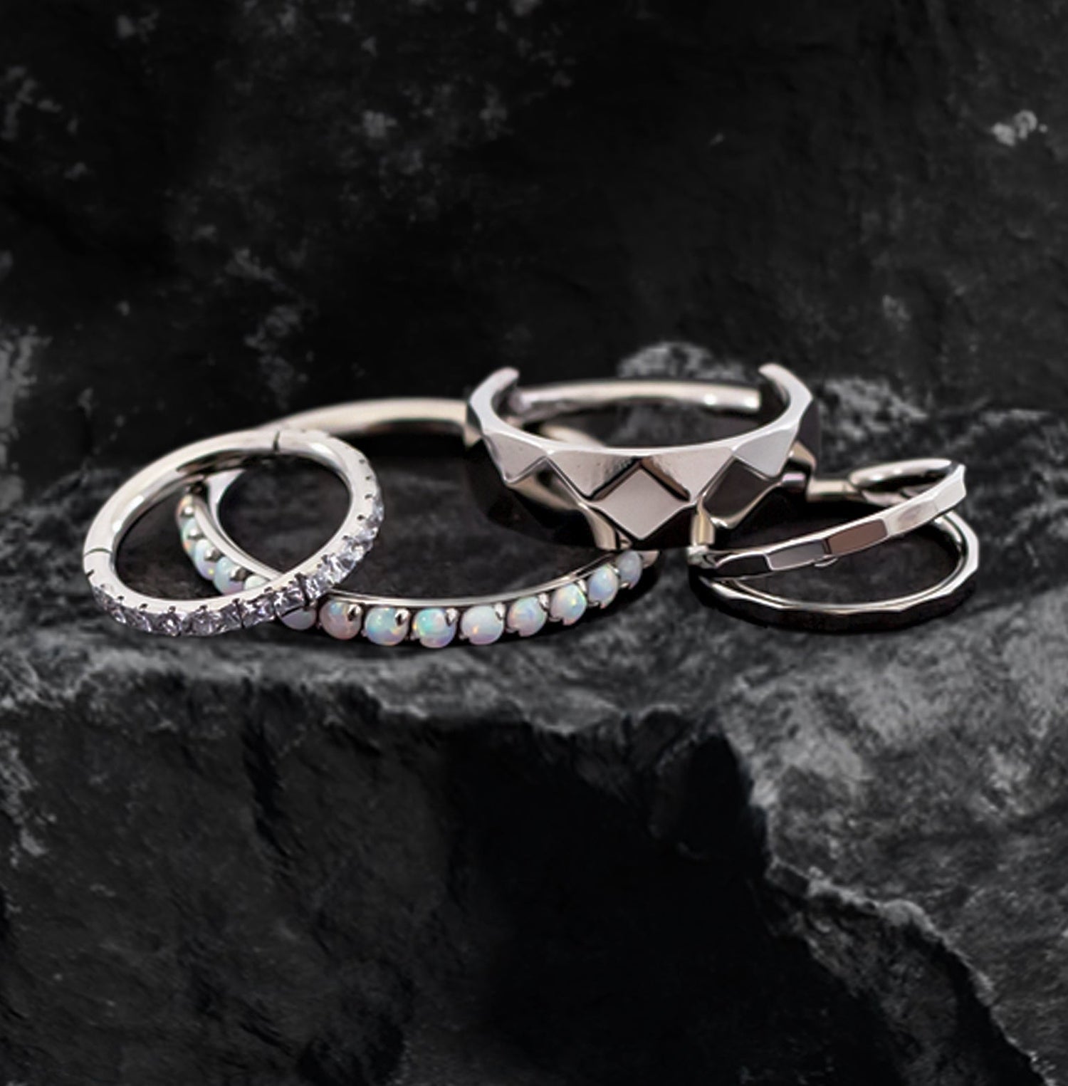 An assorted variety of titanium hinged rings with different details displayed on a black rock. 